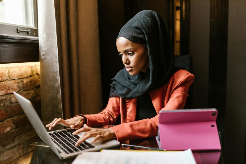 Stylish woman in hijab working on a laptop in a modern office.